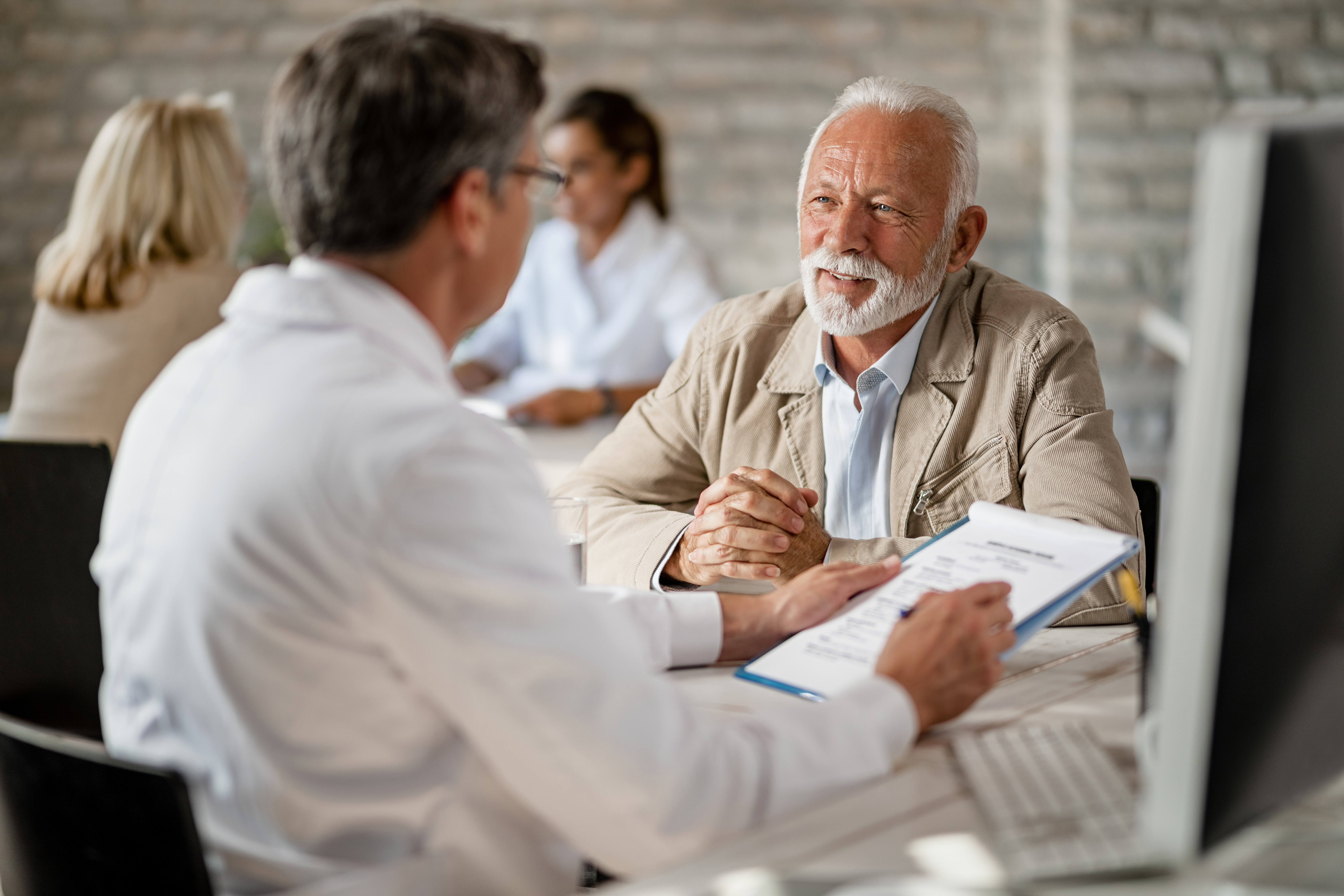 Happy mature man having consultations with a doctor about health insurance policy during a meeting at clinic.